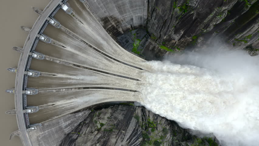 Aerial view flying downwards of extreme spillway release at Aldeadávila Dam, Spain. Massive floodgates discharge over the Douro River canyon.