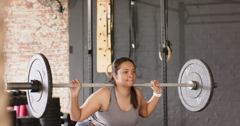 Gripping barbell and clearing rack, Hispanic woman performing back squats, building strength at gym. Strength, fitness, gym, workout, training, determination, athletic