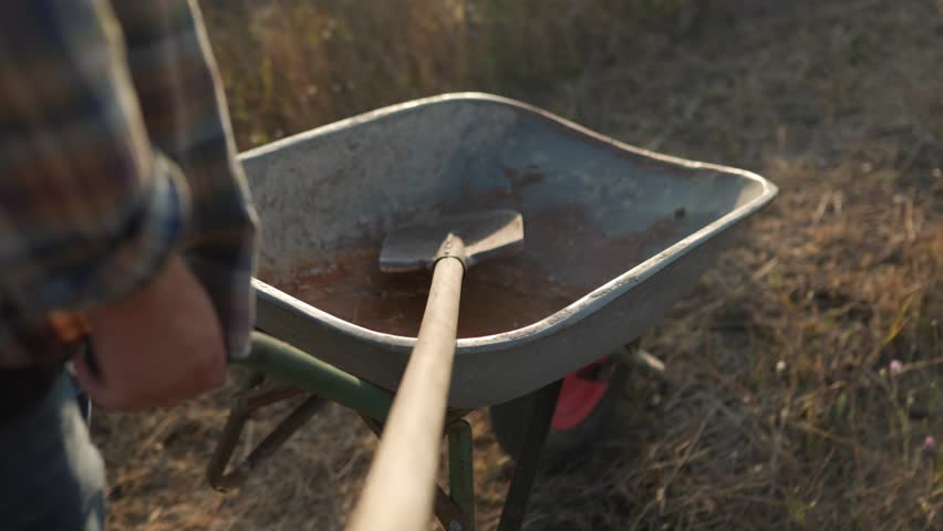 Close-up of a senior farmer legs and wheelbarrow on a rural path, emphasizing the connection to the land and agricultural life.