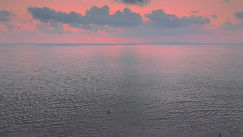 Cinematic drone shot moving backward reveals people standing on sandbank at sunset calm ocean pink sky clouds travel lifestyle freedom romance summer vacation peaceful seascape aerial view at dusk sea