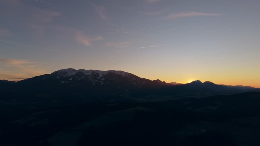 The sun touches the alpine horizon, creating a bright flare and warm gradient sky over dark hills.