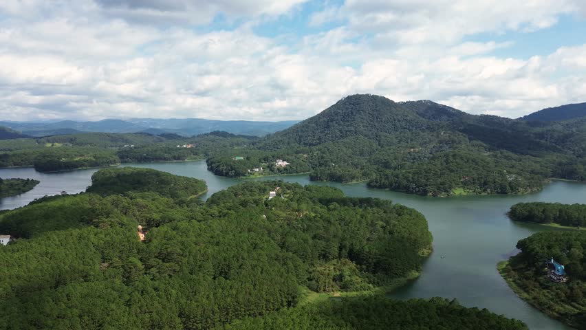 Wide aerial panorama of a highland lake branching through lush pine-covered hills with layered mountains in the background. Natural scenic landscape suitable for tourism, environment and outdoor themes.