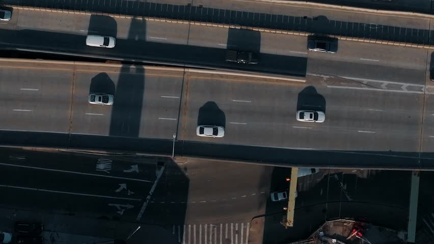 Cars move along a busy highway in New York City. The scene shows traffic on the road below with buildings and structures visible from above in daylight.