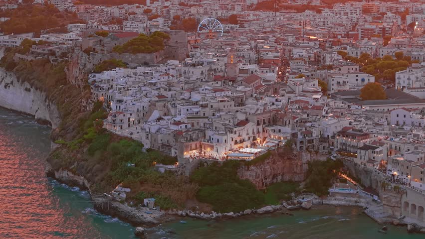 Aerial view of Vieste medieval town during a magnificent sunset in Puglia, Italy, charming resort settlement on the Mediterranean Sea with historic architecture, coastal cliffs, and warm evening light
