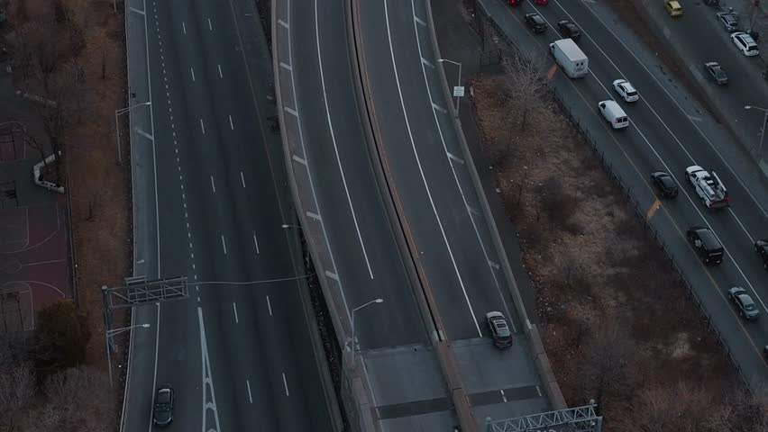 Cars move along a highway in New York during dusk. The streets are mostly clear, and buildings can be seen in the background. The scene shows city life and transportation.