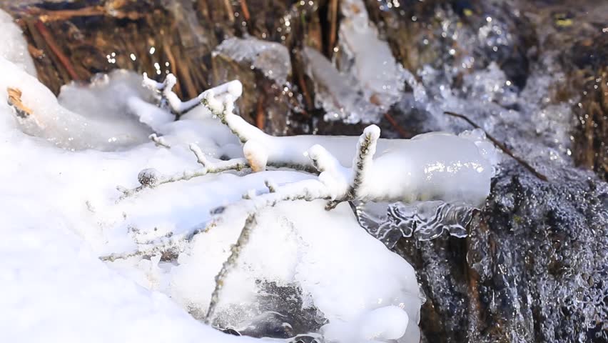 Frozen water of various shapes and textures near a waterfall. Icicles and thick layers of ice surround the cascading water, creating a dramatic winter landscape.