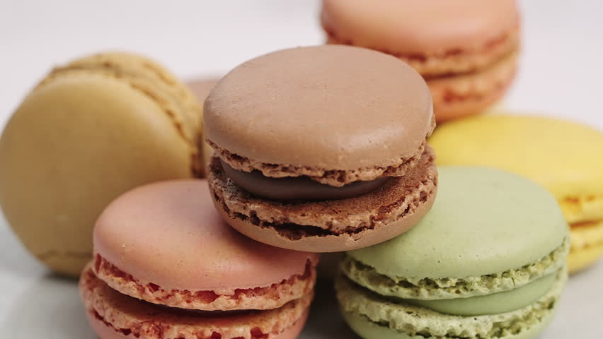 Rotating display colorful macarons assortment. Blurred balloons party decor background. Sweet snack celebration event catering service. High quality food footage birthday party theme confectionery art