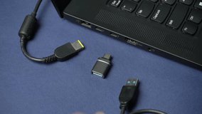 Hand reaches to connect a USB-C cable to a laptop port, with additional USB devices and cables positioned on a blue surface, creating a clear view of the workspace setup - Powered by Shutterstock - Get 15% off with code: PIKWIZARD15