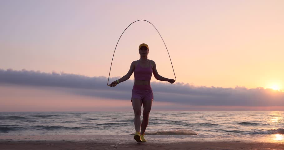 Fit young woman jumping rope at the beach. Athlete female against sea and waves background. Summer sport and healthy lifestyle concept
