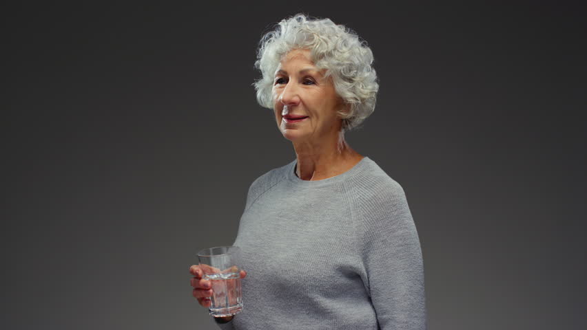 Elderly woman holding glass of water on hand, for wellness. Senior female drinks water, hydration. Old person, drinking beverage. Retirement with liquid, fluid and minerals, hydration and detox