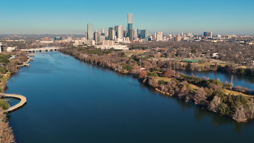 Crisp morning drone footage over Lady Bird Lake highlighting a wooded peninsula in East Austin with downtown Austin’s skyline rising beyond the Colorado River. Walking trails wind through parkland while calm water defines the shoreline. Ideal for urban lifestyle, relocation, travel marketing, sustainability, and Texas city growth concepts.