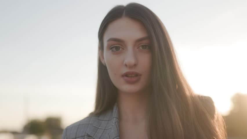 A young brunette woman face beautifully illuminated by the setting sun in this close-up portrait, exuding elegance and beauty.