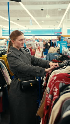 A young beautiful woman selects clothes for her boyfriend in a clothing store something catches her attention and she examines it carefully.