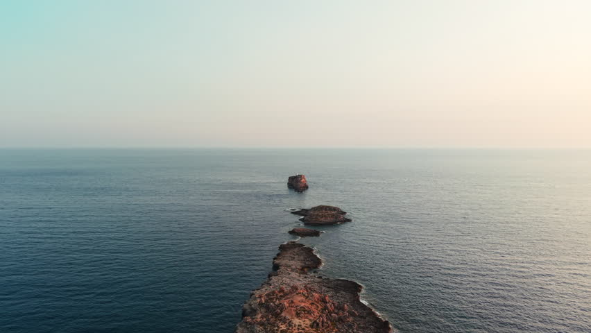 Rocky islet emerging from the calm mediterranean sea at cala toro, in favignana, aegadian islands, sicily, italy