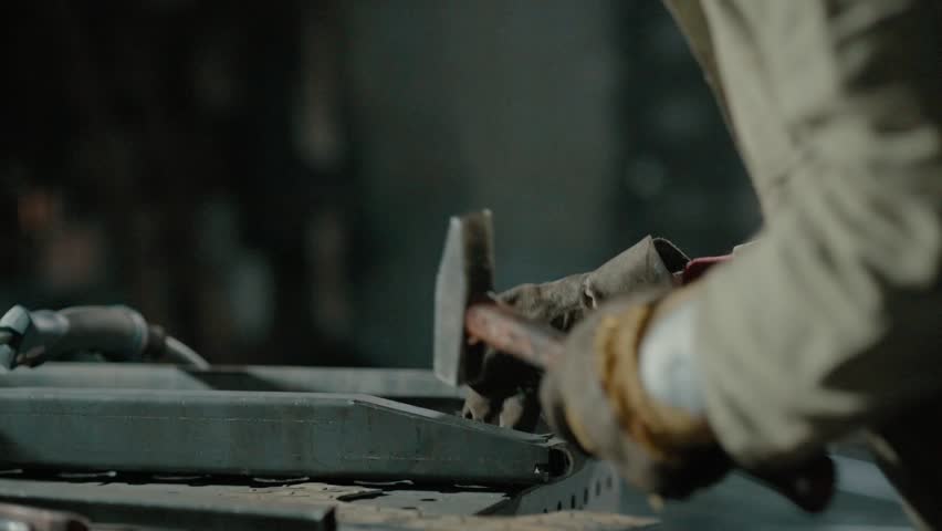 Locksmith hits a metal part with a hammer, work in a workshop. Close up of hands, slow motion.