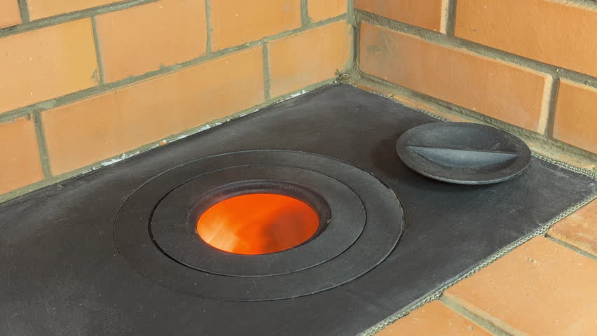 A cooktop of a newly built heating stove. The burner rings are removed, the flame in the firebox is visible. Close-up