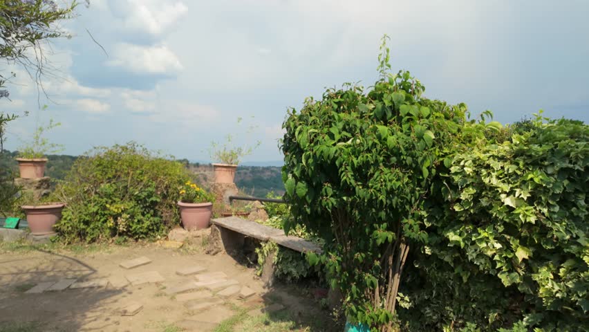 Expansive view of the unique Calanchi badlands, featuring deeply eroded hillsides and vibrant green vegetation, seen from a high vantage point with a foreground garden.