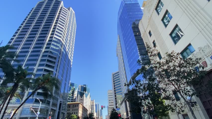 Low Angle Pan of Skyscrapers and Office Buildings in Sunny American Downtown. Smooth low-angle view of towering skyscrapers in a modern American city. Office buildings reach towards a clear blue sky on a bright sunny day. Concepts of business, success, and urban growth.