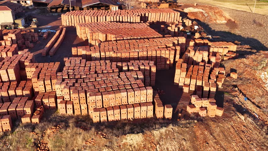 Red construction bricks neatly stacked in an open-air warehouse. Building materials and industrial stock concept in the light of sunset.