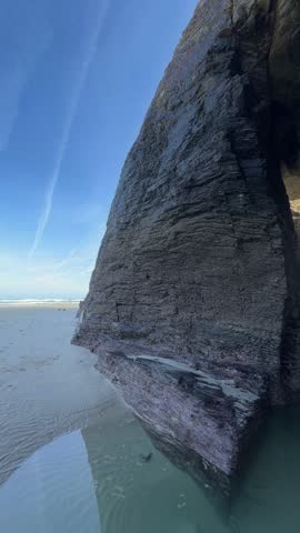 Vertical footage showing steep coastal cliffs rising above greenish ocean water at Playa de las Catedrales. 
