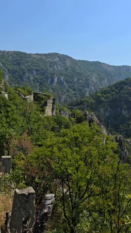 Mountain landscape in Bulgaria with forested hills and rocky slopes surrounded by lush green trees under clear blue sky creating scenic summer nature view