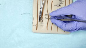  Surgical Suturing Practice on Silicone Skin Model Close Up. Close-up of blue gloved hands performing suturing on a silicone skin training pad using surgical instruments. Medical student practicing wound closure during clinical skills training. - Powered by Shutterstock - Get 15% off with code: PIKWIZARD15