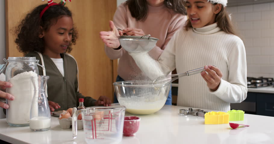 Diverse family mixing holiday treats on kitchen counter, mother sifting flour as daughter whisking. Festive, family, baking, celebration, warmth, tradition, home