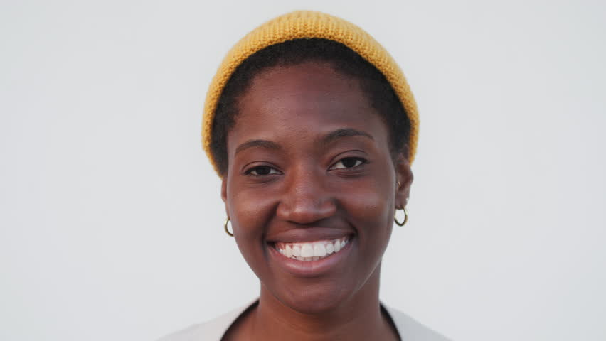 Zoom in shot of woman in yellow cap standing against white background. Smiling female looking at camera on plain background