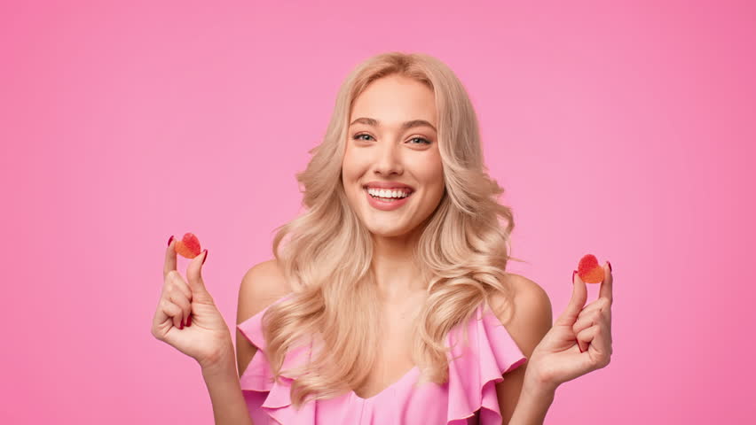 Woman With Blonde Hair Smiles While Holding Candy in Front of a Pink Background