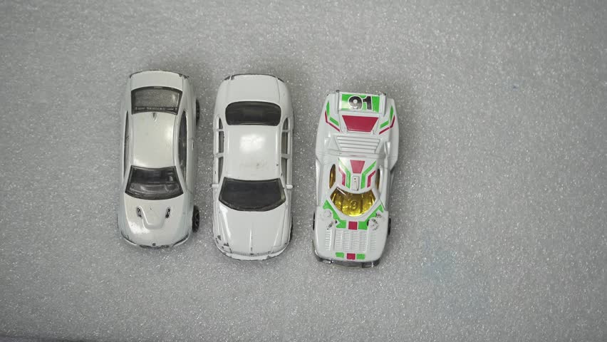 A closeup of three white toy cars parked on a white table as a red car approaches them representing inclusion and equality. 