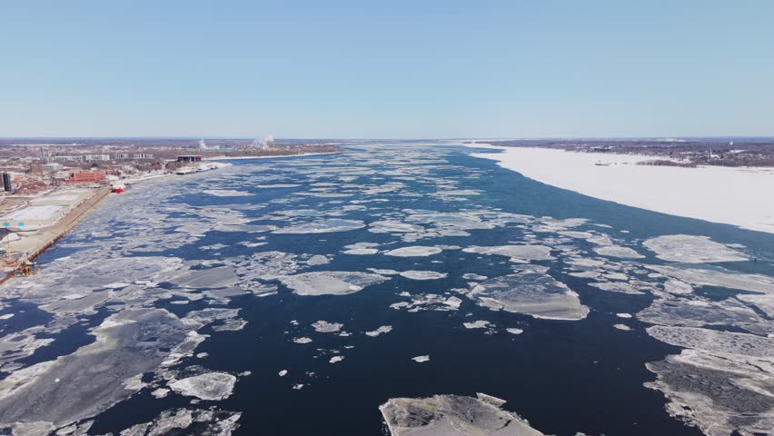 Wide drone shot of partially frozen river with ice plates and open water.