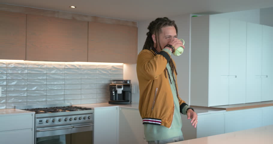 Man in mustard jacket walking into kitchen, picking green mug and sipping coffee while laughing. Modern, lifestyle, candid, cozy, warmth, casual, interior