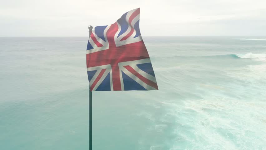 Gusts of wind increasing, Union Jack flag on pole curling, folding, snapping outward over ocean. Banner, ensign, coastal, seascape, horizon, overcast, motion