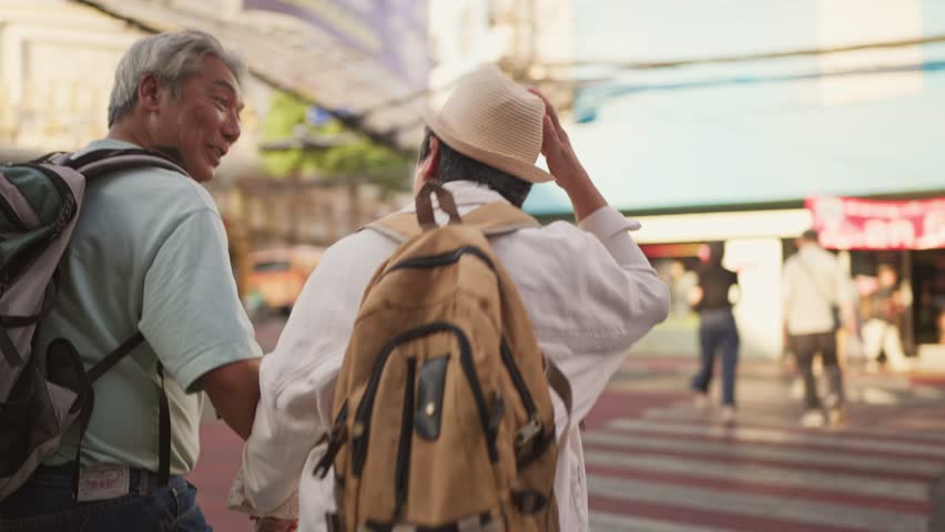 Asian senior couple traveler traveling and exploring the city outdoors. Elderly man and woman tourist walk along street, enjoy leisure time urban travel and joyful experience during holiday vacation.