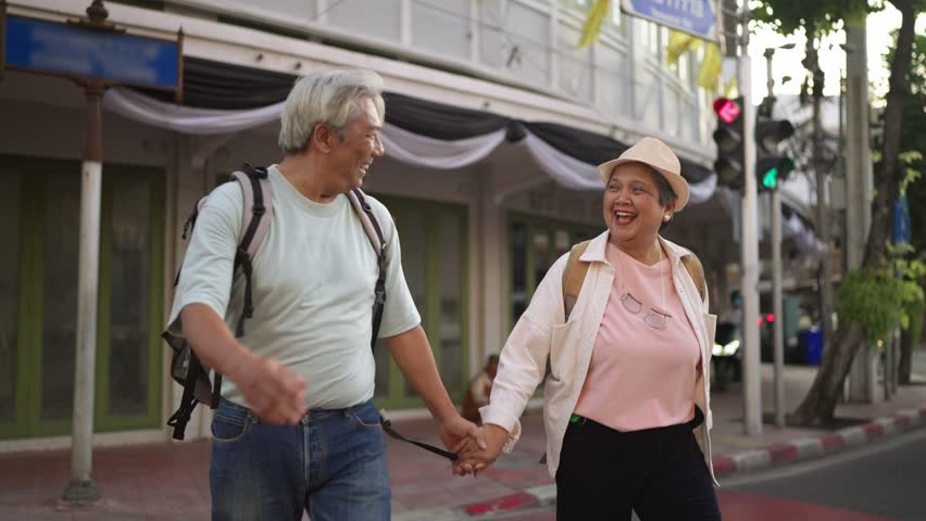 Asian senior couple traveler traveling and exploring the city outdoors. Elderly man and woman tourist walk along street, enjoy leisure time urban travel and joyful experience during holiday vacation.