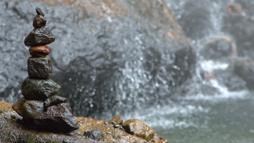 A static medium shot captures balanced rocks beside a rushing waterfall in Ngardmau, Palau