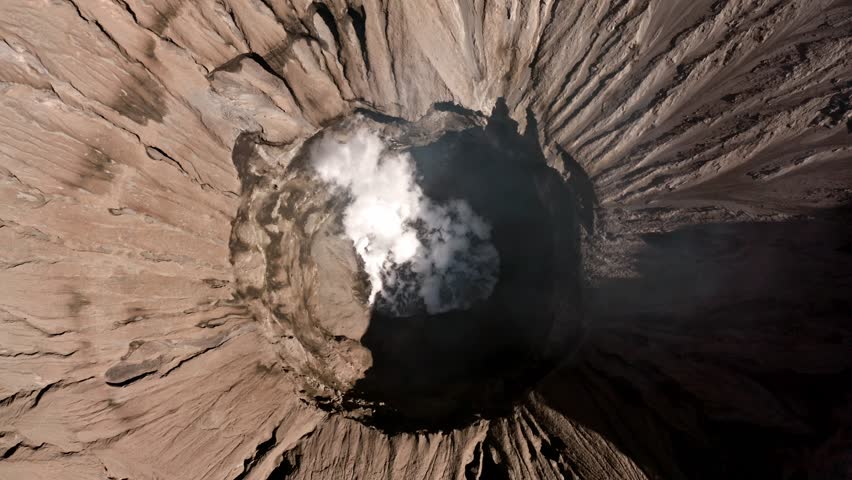 Top View Into Active Crater of Volcano Mount Bromo In East Java Indonesia. Volcano White Smoke Rising From Depth Showing. Breathtaking Aerial Looking Power of Nature and Geology Background Concepts 4k