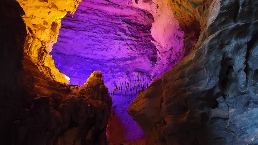 Stunning interior of a limestone cave in Zhangjiajie featuring vibrant purple and orange artificial lighting on stalactites and rock walls.