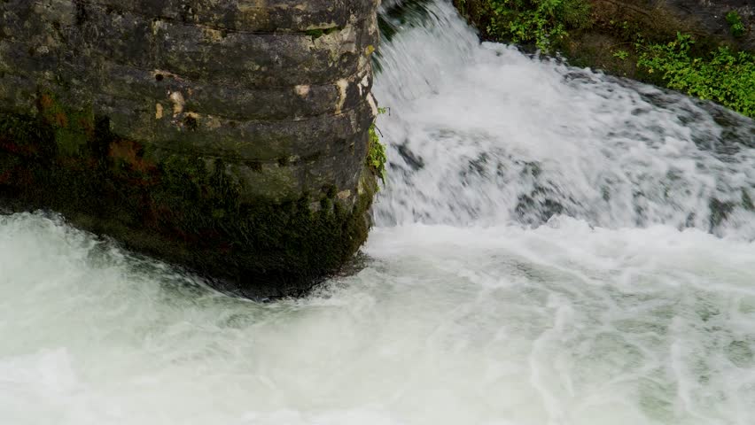 Close up view of a small section of the river Cheddar Yeo divided by a round brick wall, water running down and making white foam. Cheddar Yeo a small that runs under the limestone of Mendip hills.