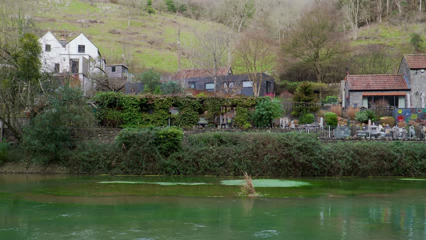 Cheddar Yeo a small river in Somerset. Beneath the limestone of the Mendip Hills it forms the largest underground river system in Britain. River slowly flowing with houses and hills in the background.