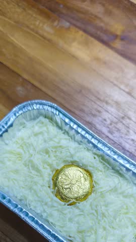 Snow Cheese Cake or Klappertaart Dessert in Aluminum Foil with Generous Grated Cheese and Gold Wrapped Topping on Wooden Table