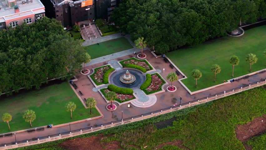 Aerial view of people and pineapple fountain in waterfront park of downtown Charleston, South Carolina skyline cityscape and lowcountry landscape with local architecture along scenic water - 4K Drone