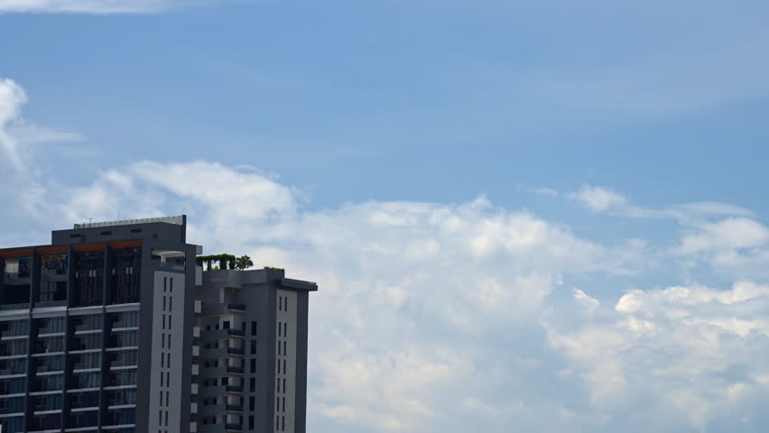 Daytime timelapse capturing the movement of clouds across a bright blue sky, set against the architecture of a modern high-rise residential building.