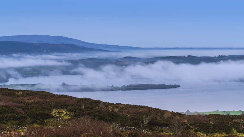 Timelapse of rural landscape with fog inversion above lake in distance and hills beyond viewed from Carrowkeel in county Sligo in Ireland.