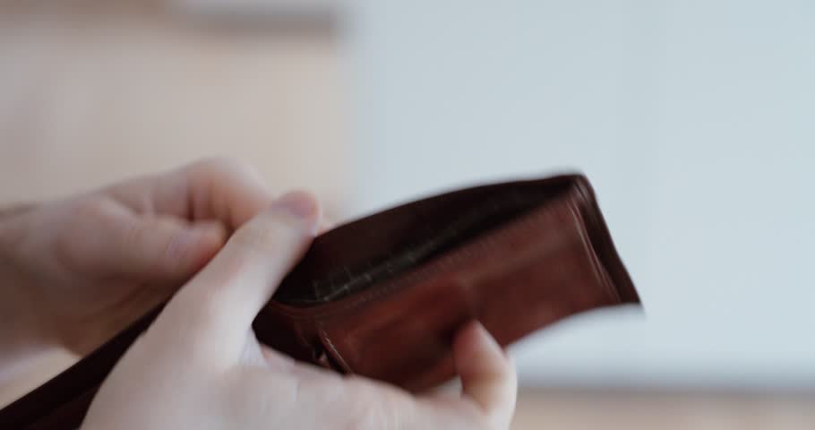 Close-up of a man opening an empty wallet with no money inside. Concept of financial stress, debt, poverty, economic crisis and personal money problems.