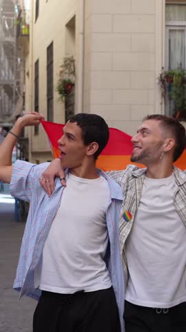 Cheerful young gay couple embracing and holding a rainbow flag during a pride parade. Slow motion video celebrating love and equality