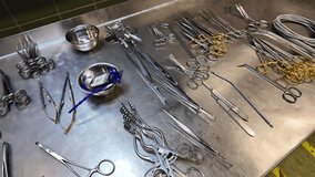 Close-up view of sterile surgical instruments neatly arranged on a stainless steel table in a hospital operating room. The image shows forceps, scissors, clamps, needle holders - Powered by Shutterstock - Get 15% off with code: PIKWIZARD15