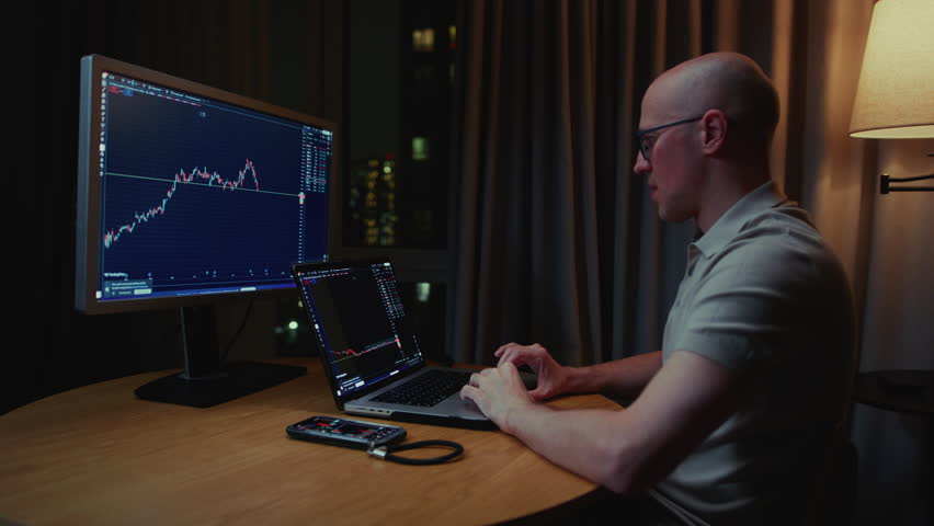 Man in trader home office. Monitor and laptop are on table. Trading program or exchange. Male analyzes candlestick charts for crypto market. Managing Investment portfolio, monitoring financial data