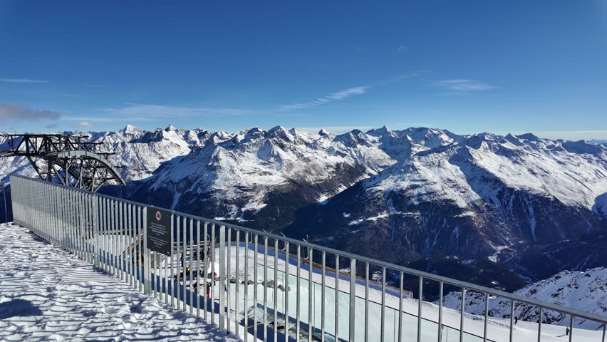 Wide panoramic winter landscape of the ski resort in Sölden, Austria, captured under bright alpine sunshine. The image shows a high-altitude glacier slope in the Ötztal Alps with ski lifts