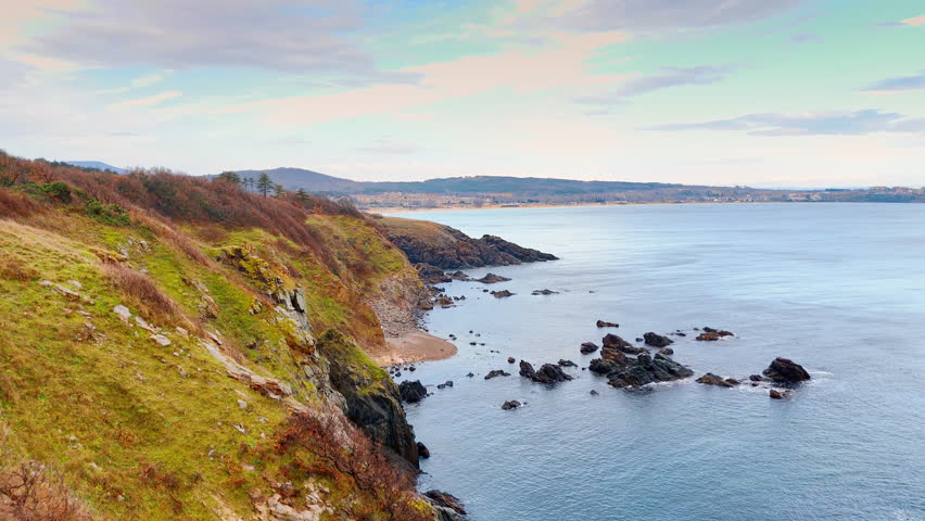 Elevated view of a rocky bay and sandy beach. High angle shot of a coastline featuring rocky outcrops, a small sandy patch, and a distant coastline.